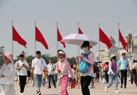 Getty Images Tourists use umbrellas and protective clothing to shade from the sun at Tiananmen Square as the city temperature reaches 40C on Beijing, China.