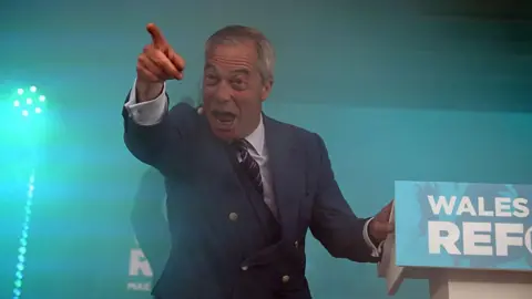 Getty Images Nigel Farage stood at a lectern, pointing to the crowd and making a 