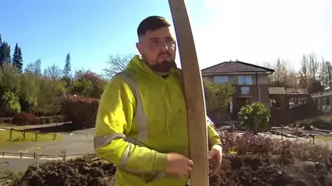 Lancashire County Council A man in a yellow workers' jacket while holding a large pole stood outside a residential home on a sunny day. 