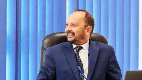 Royal School for the Deaf Derby Man smiling in navy suit and tie.