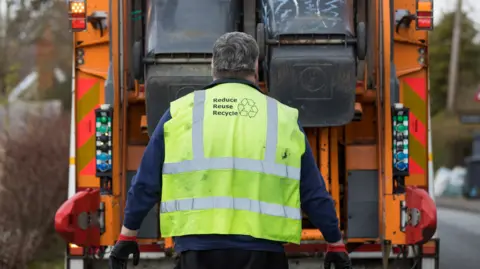 Bin collector loading bins on a lorry an wearing a council fluorescent vest