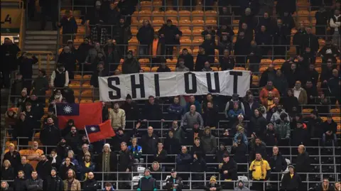 Getty Images Fans at a fairly empty Molineux stadium unfurl a banner saying "Shi Out" during the game against United.
