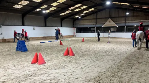 Leanne Rinne/BBC The East Park Riding for the Disabled Group, on East Park Lane in Lingfield, Surrey. A number of ponies trotting on sand can be seen in the picture. 