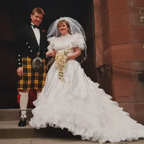David Swift Photography Kenny (left) and Lisa pictured after their wedding ceremony. They are hoolding hands as they stand on the church's steps. Kenny has brown hair and is wearing a black jacket and yellow kilt. Lisa is wearing a white gown with long train and holding a bouquet of flowers.
