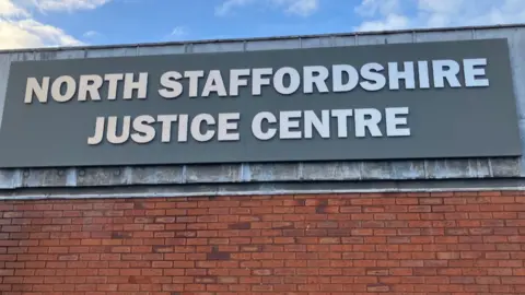 A large grey sign over a red-brick wall says North Staffordshire Justice Centre.