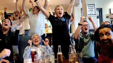 Football fans jumping for joy in a pub. 