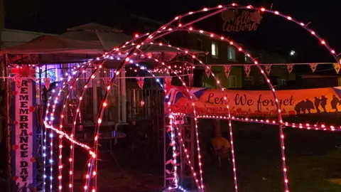 Sandra Lee Myles A tunnel of red lights for Remembrance Day. A Lest We Forget banner is hung on the left and a Remembrance Day banner on the right.