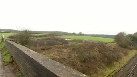 A bridge over a rail track with fields in the background