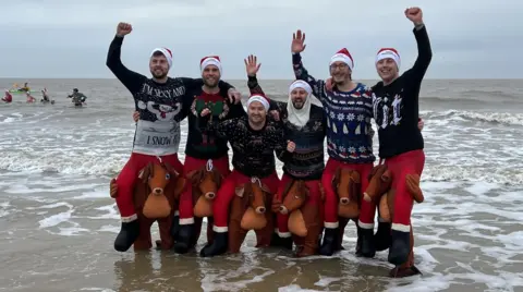 Matt Stebbings Six men dressed in Christmas jumpers and in reindeer fancy dress outfits in the sea