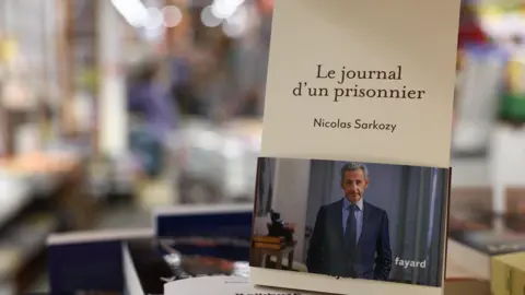 Reuters A copy of former French president Nicolas Sarkozy’s memoir "Journal of a Prisoner" (Le journal d'un prisonnier), which details his time in prison after being jailed for criminal conspiracy, is displayed in Paris, France, December 10, 2025.