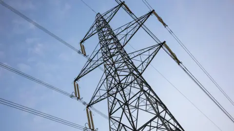 Getty Images An electricity pylon against a blue sky with tiny clouds.