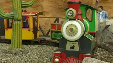 A choo choo train ride for children with a big plastic cactus and boulders