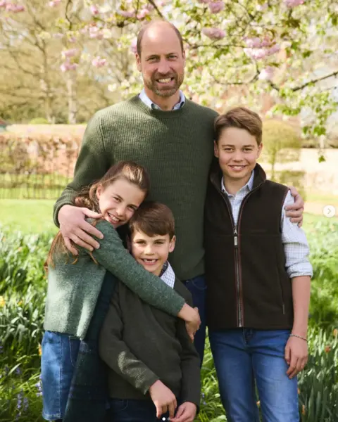Josh Shinner A portrait image of Prince William with George, Charlotte and Louis standing against a garden. All four look towards the camera and smile.
