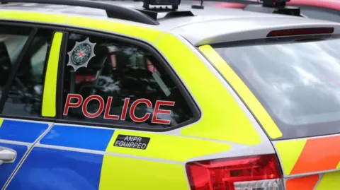 PA Media A police car which is yellow and blue in colour. Police is written on the side in red letters.