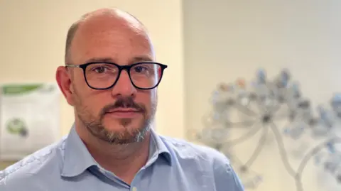 Dr Graeme Fitzpatrick is a bald man in dark glasses, wearing a blue shirt, open at the collar