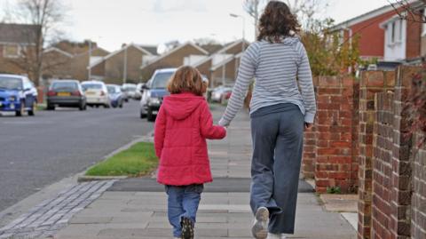 Rear view of a woman and a young girl walking on a residential street holding hands