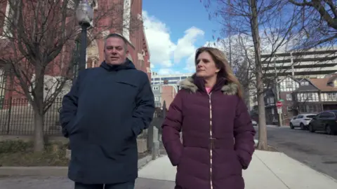 Ellen Roome and Liam Walsh walking a street in the U.S. Both are wearing winter coats.