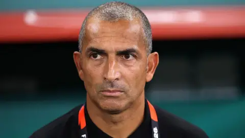 Close up of Sabri Lamouchi standing in the dugout looking focused