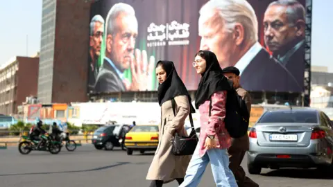 EPA Iranians walk past an anti-Israeli and US billboard depicting pictures of Iranian president Masoud Pezeshkian and Iranian Islamic Revolutionary Guard Corps military commander General Mohammad Bagheri in Tehran, Iran. October 2024