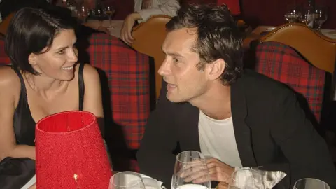 Dave Benett/Getty Images Sadie Frost in a black dress smiles as she looks across at actor Jude Law, who's seated next to her at an after party at the Dorchester in 2006. 