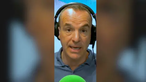 A man, Martin Lewis, wearing headphones, looking at the camera, with a green mic in front.