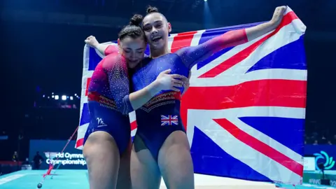 The Gadirova twins are dressed in red and blue leotards and holding the union flag behind them at the World Gymnastics Championship.