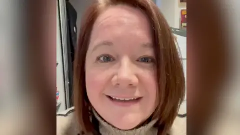 Laura Betts A woman with brown, straight, shoulder‑length brown hair that curves slightly inward at the ends smiles into the camera. She is wearing a light‑coloured, high‑necked sweater. 