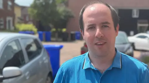 George King/BBC A head and shoulders image of Andy McGowan. He is wearing a blue polo short and standing in a residential street. He is looking directly into the camera.