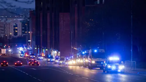 Merseyside Police A convoy of yellow police vans drive up a hill in the early hours of the morning
