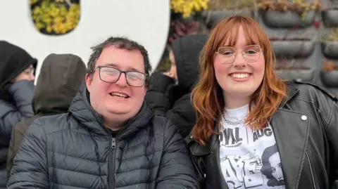 A young man and a young woman stand smiling at the barrier outside of Co-op Live.