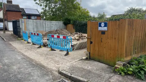 BBC/Danny Fullbrook Material from patio work stored at the back entrance to St Mary's House which is a wooden fence attached to a wooden fence.