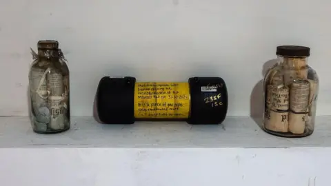 Derby City Council Two time capsules in glass bottles, dating from 1864 and 1938, next to a yellow time capsule from 2024