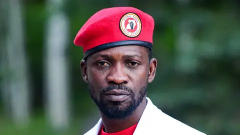 Bobi Wine looks directly at the camera wearing a red beret, a red t-shirt and a white blazer