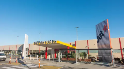 The departures entrance at Avalon Airport in Melbourne Australia, with a Jetstar logo on the side and a blue sky in the background