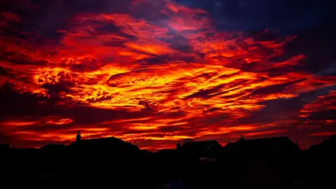 BBC Weather Watchers/Olly A red, orange and yellow swirly sky which looks like lava. Houses cast in shadow are visible below.