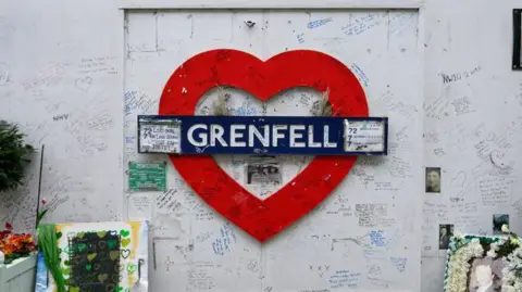 Grenfell Tower memorial with a red heart, tribute messages, flowers, and photos honouring victims