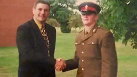 Ross Coombs Ross is dressed in his army uniform shaking hands with his father Jon who is dressed in a suit and tie.