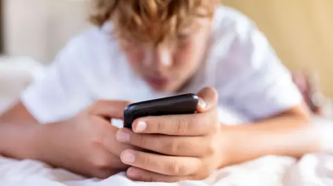 Getty Images A teenage boy, lying on his bed wearing a white t-shirt and using a mobile phone