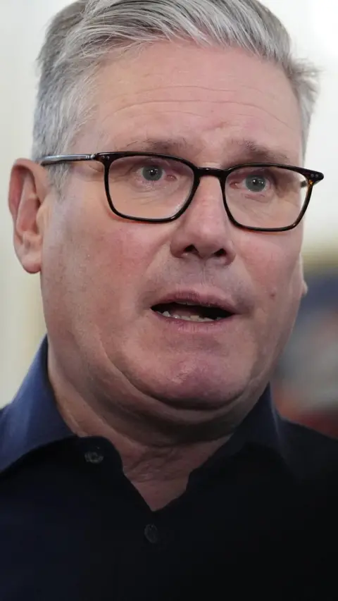 The prime minister, wearing a dark shirt and dark rimmed spectacles, answers a question