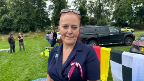 Kate Bradbrook/BBC Beckie Ramsay with long brown hair wearing a purple top and a red and white ribbon