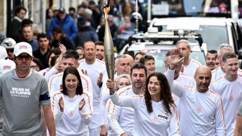 Members of the public look at a torch bearer holding the Olympic Torch as part of the Olympic and Paralympic Torch Relays, ahead of the Paris 2024 Olympic and Paralympic Games, in Saint-Emilion, southwestern France on May 23
