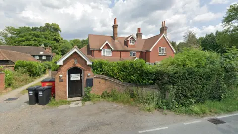 A large brown brick house behind green hedges
