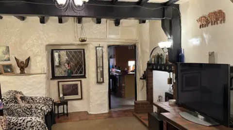 The living room with has all white walls with cave-like texture. There are two chairs with leopard print in front of a large flat screen television.