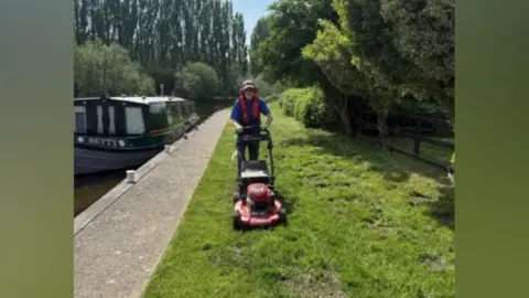 Canal & River Trust Brian Orwin pushing a lawnmower by a canal 