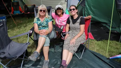 Anita Rani with a mother and daughter outside a tent