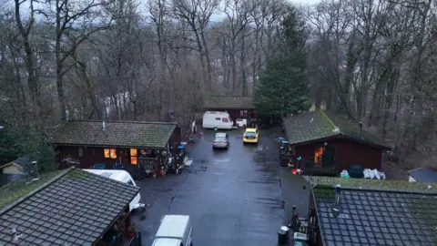 An aerial view of five cabins with cars and a caravan parked outside
