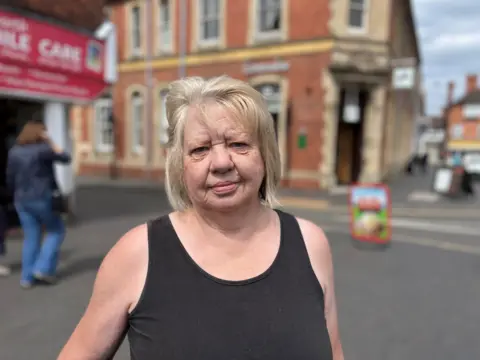 A woman with a black top and blonde hair standing in a street