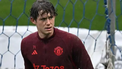 Tom Wooster wearing a red Manchester United warm-up shirt