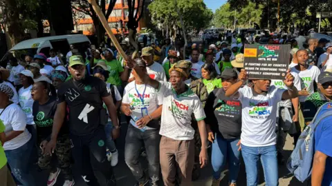 BBC / Thuthuka Zondi A shot of the march from in front. People are chanting and one man is holding a sign.