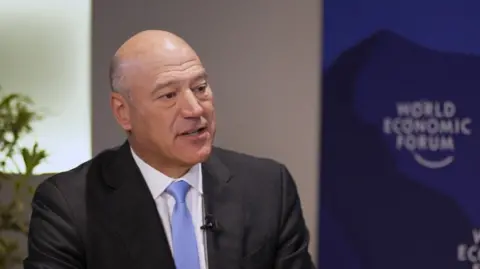 Gary Cohn wearing a dark grey suit, white shirt and pale blue tie being interviewed in front of a sign saying World Economic Forum